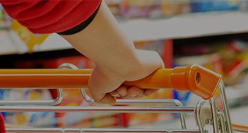 hand pushing a shopping cart in a supermarket lane with consumer goods in the background